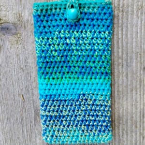 Etui-ochraniacz na telefon w kolorach turkusu i niebieskiego. Zapinane na drewniany koralik.