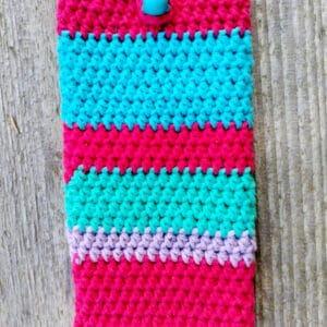 Etui na telefon w paski w intensywnych kolorach czerwieni, turkusu, zieleni i jasnego fioletu. Zapinane na drewniany koralik